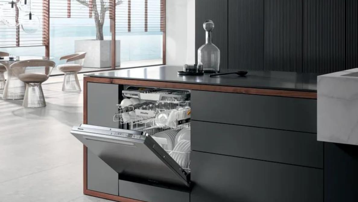 An image of a modern kitchen that includes the Miele dishwasher. Its door is open, revealing its inner racks stocked with spotless dishes.