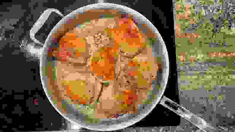 Several seared chicken thighs inside of stainless steel pan on top of cooktop.