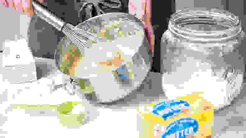 A person uses a whisk to stir cake batter in a metal mixing bowl.