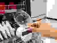 A hand holding up a dry, spotless glass in front of a Bosch dishwasher