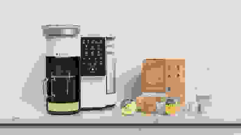 Bruvi coffee machine with mug full of coffee under dispenser next to box of coffee pods on marble countertop.