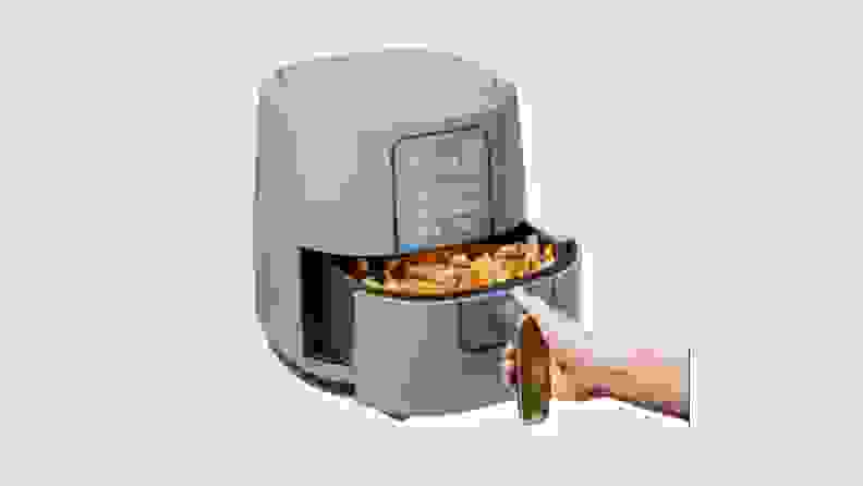Hand pulling out basket on the light blue air fryer from the Beautiful by Drew Barrymore Kitchen Appliances line.