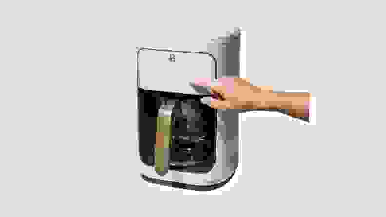 Person using finger to power on lavender-colored coffee maker from the Beautiful by Drew Barrymore Kitchen Appliances line.
