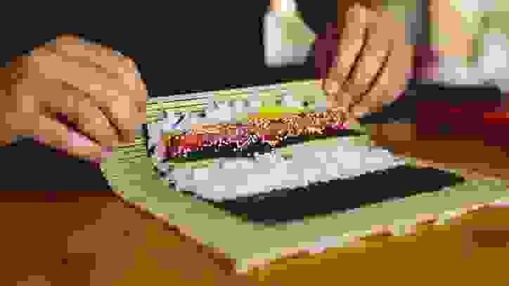 person using sushi mat to roll sushi