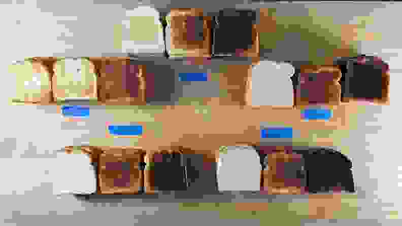 15 pieces of toast with varying browning laid out on a countertop with distinguishing labels from respective toaster brands.