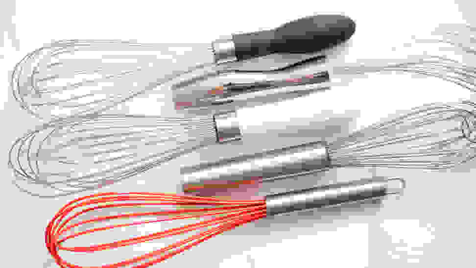 Assorted whisks arranged on a marble countertop.