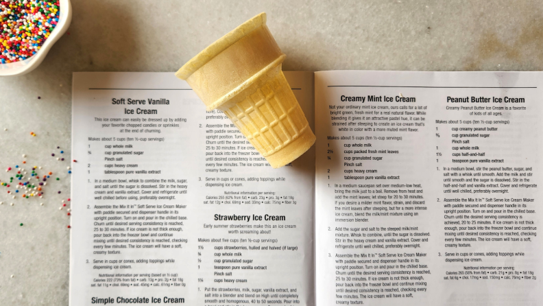 An empty ice cream cone sitting on top of an instruction manual next to a bowl of sprinkles.