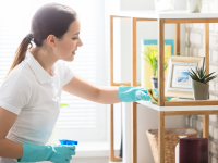 Woman wearing blue rubber gloves and spray bottle to wipe off surface in home.
