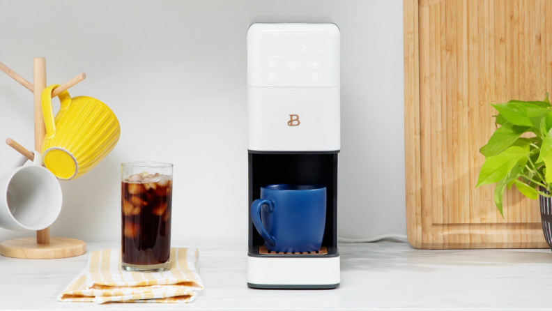 The coffee maker with a blue mug in it and a cup of iced coffee next to it.