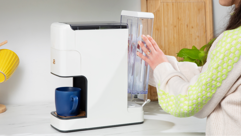 A person installing the refillable water tank into the coffee maker.