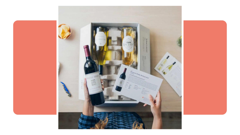 A person of holding a bottle of Firstleaf Wine and an informational card above a box of other wines.