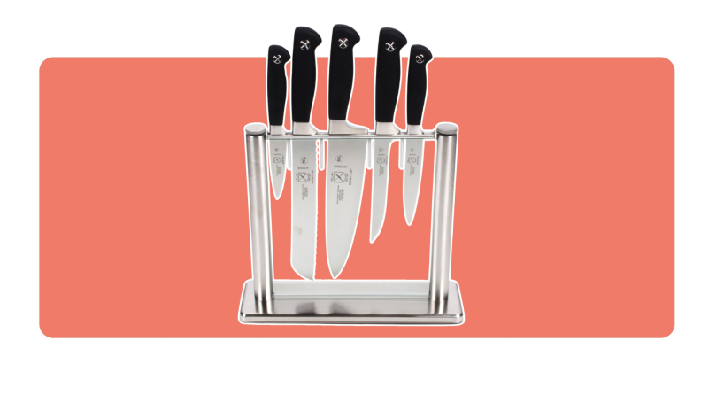 A 6-piece set of Mercer Culinary knives set in a glass knife block, on a peach background.