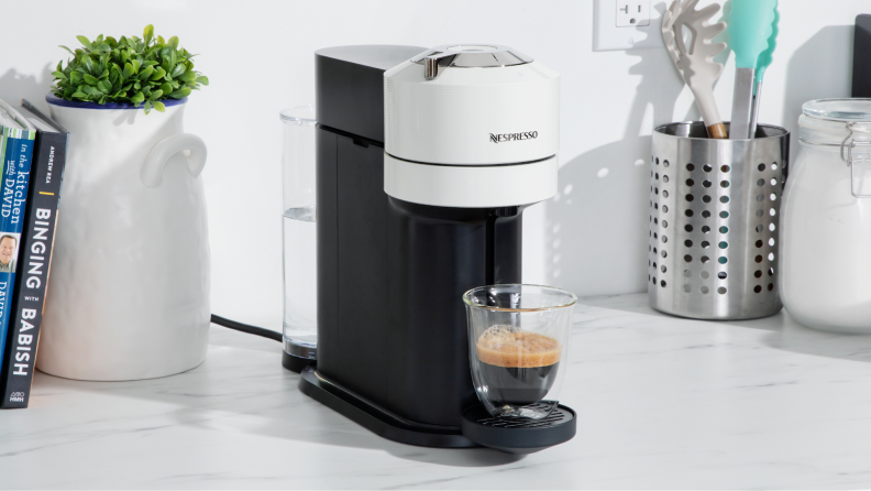 Nespresso Vertuo Next coffee maker on marble countertop next to potted plant and kitchen utensils.
