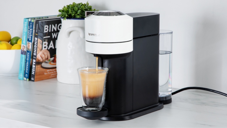 Nespresso Vertuo Next coffee maker on marble countertop next to potted plant and kitchen utensils.
