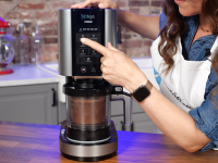 A person pressing a button on the Ninja Creami ice cream maker, with chocolate ice cream in the pint container.