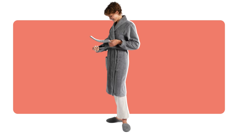 A model smiles while looking down as they adjust the straps on their gray Parachute Classic robe.