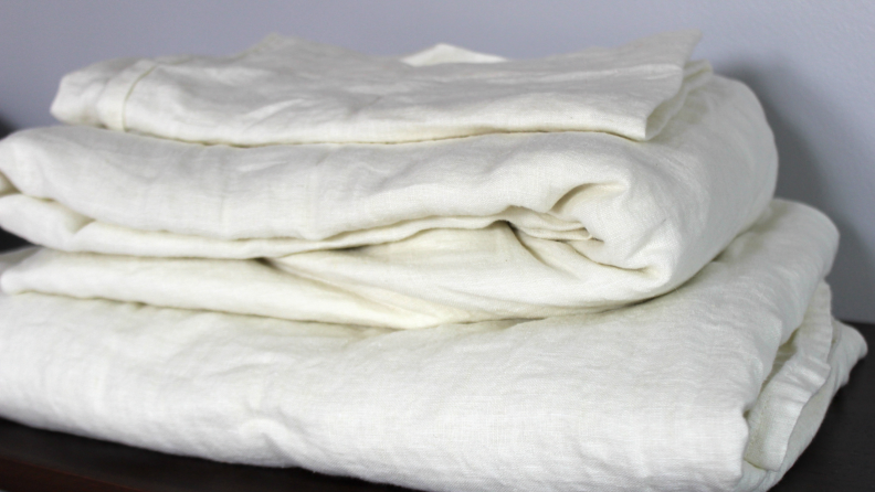 Cream linen bed sheets from Saatva—the best linen bed sheets we tested—lie folded in a stack.
