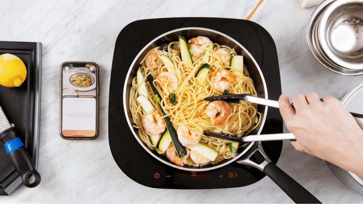 A hand scooping some shrimp noodles from the Tramontina Guru cookware.